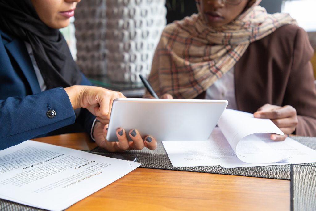 Female professionals working on documents. Young Muslim business women sitting in cafe, reading papers and using tablet. Business meeting or partnership concept
